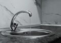 Chrome faucet with running water in a modern kitchen with marble countertop.