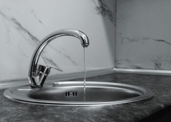 Chrome faucet with running water in a modern kitchen with marble countertop.