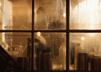 Moody view through a fogged window into a cozy interior with warm lighting.