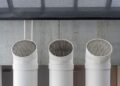 Three white industrial ventilation pipes aligned on concrete wall.
