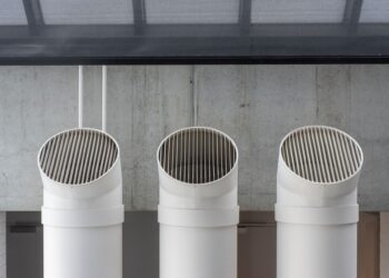 Three white industrial ventilation pipes aligned on concrete wall.