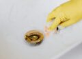 From above of crop anonymous person in yellow rubber protective glove using sponge and detergent for washing white sink in bathroom