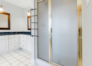 Elegant bathroom featuring a shower with gold trim and marble countertops, highlighting modern interior design.