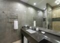Spacious modern bathroom featuring granite countertop, glass shower, and stainless steel fixtures.