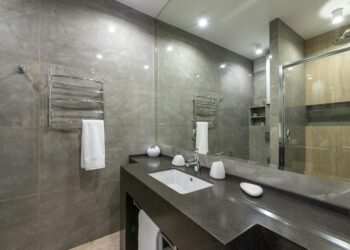 Spacious modern bathroom featuring granite countertop, glass shower, and stainless steel fixtures.