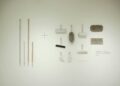 A minimalist flat lay of various cleaning tools arranged on a white wall, showcasing a modern concept.