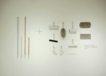 A minimalist flat lay of various cleaning tools arranged on a white wall, showcasing a modern concept.