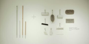 A minimalist flat lay of various cleaning tools arranged on a white wall, showcasing a modern concept.