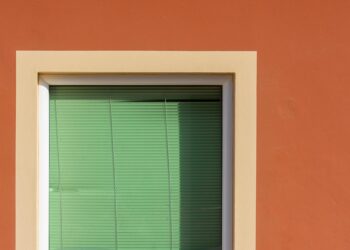 A minimalistic view of a green window with blinds set in an orange wall, creating a vibrant contrast.
