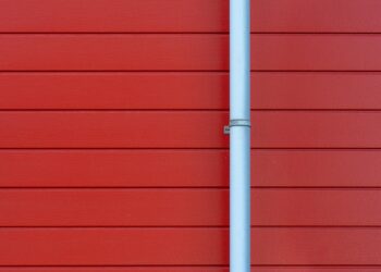 A minimalist photo of a red wall with a white rain gutter, showing clean lines and vibrant color contrast.
