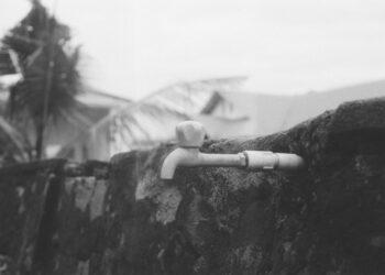 Monochrome image showing an outdoor water faucet mounted on a stone wall.