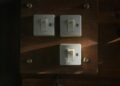 Close-up view of vintage light switches mounted on a wooden panel, illuminated softly in a dark interior setting.