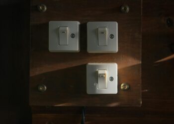 Close-up view of vintage light switches mounted on a wooden panel, illuminated softly in a dark interior setting.