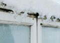 Sharp icicles hang from a window frame, covered in snow, showcasing winter's beauty.