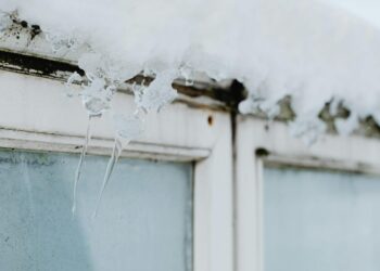 Sharp icicles hang from a window frame, covered in snow, showcasing winter's beauty.