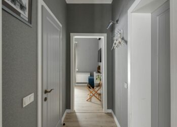Spacious hallway with grey walls, wooden doors and white hangers, leading into a modern room.