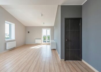 Spacious empty room with wooden flooring and large windows for ample natural light.