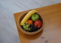 Vibrant assortment of fruits in a woven basket on a wooden tabletop.