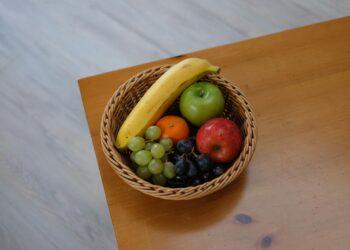 Vibrant assortment of fruits in a woven basket on a wooden tabletop.