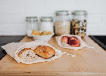 Wooden kitchen counter displaying bread and fruits in reusable bags for a zero-waste lifestyle.