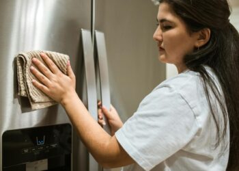 A woman wipes a refrigerator with a cloth, focusing on maintaining cleanliness in a kitchen.