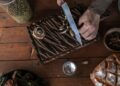 Top-down view of hands slicing mushrooms on a cutting board. Rustic wood setting.