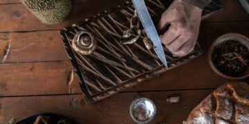 Top-down view of hands slicing mushrooms on a cutting board. Rustic wood setting.