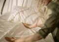 A person arranging bed linens in a warm, sunlit bedroom, creating a cozy and inviting atmosphere.