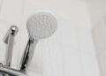 Stylish clean shower head with water flow in a white tiled bathroom.