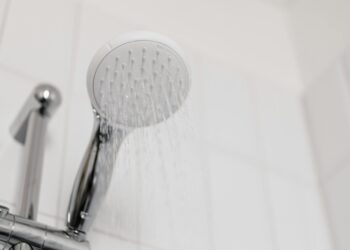 Stylish clean shower head with water flow in a white tiled bathroom.