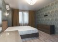Interior of bedroom with air conditioning above bed placed near window with curtains and dresser