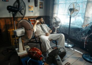 Man in white suit relaxing amongst multiple fans in a retro-themed room.