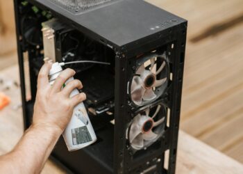Crop anonymous male with compressed air can removing dust from computer system unit