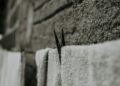 Black and white close-up of towels drying on a wall, featuring a clothespin.