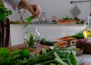 Hand preparing herbs and vegetables in a kitchen setting. Fresh ingredients on a rustic table.