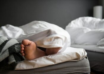 A close-up of a bare foot poking out from under a soft duvet in a modern bedroom.