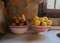 Colorful bowls filled with fresh bananas, apples, and lemons on a rustic kitchen counter.