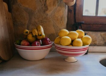 Colorful bowls filled with fresh bananas, apples, and lemons on a rustic kitchen counter.