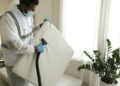 Man in protective gear vacuuming a mattress in a modern home interior.