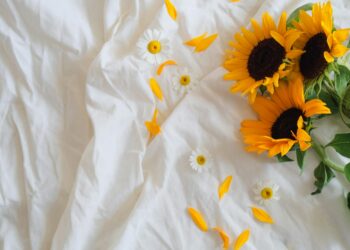 Vibrant sunflowers and daisies lie on smooth white bedding, capturing a sense of tranquility.