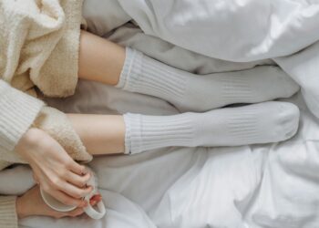 Relaxing indoors wrapped in white linens and warm clothing, enjoying a soothing moment with a cup.