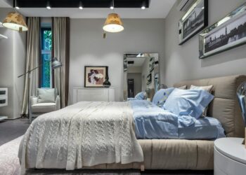 Interior of contemporary cozy light bedroom with comfortable bed with knitted plaid and bedclothes beige silk curtains and pictures on wall