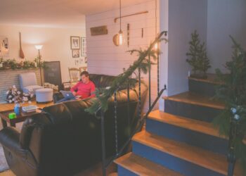 A cozy living room adorned with holiday decor, featuring a person working remotely on a laptop.