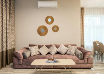 Comfortable sofa with cushions placed near table with magazines in lounge in daytime