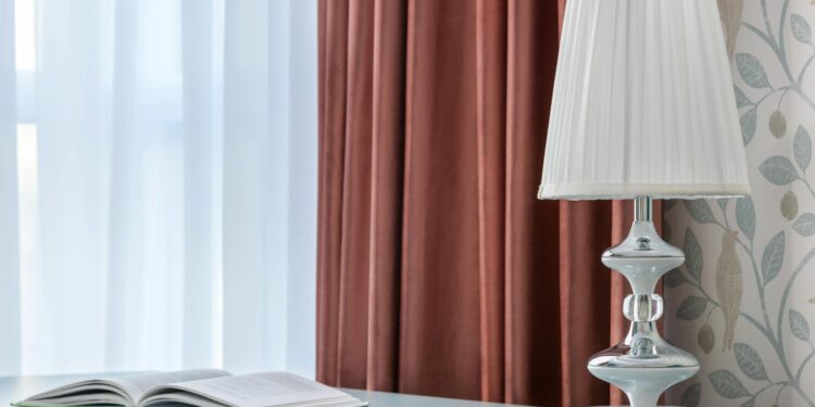Decorative lamp and open textbook on smooth table against curtains and wall with bird ornament in light house