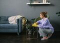 Side view of young female in latex gloves squatting down and wiping table in stylish living room in daytime