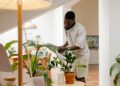 Man tending to houseplants in a bright modern living room setting.