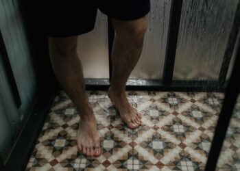 Close-up view of a person standing with wet feet on a tiled shower floor.