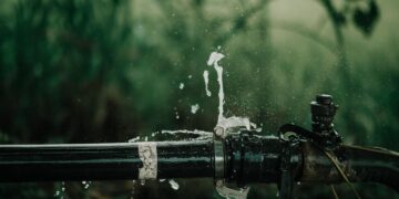 A detailed view of a leaking water pipe in a lush green garden setting.