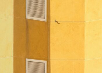 Close-up of a modern yellow building corner featuring ventilation grilles for architectural interest.